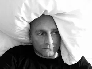 A man battling the flu, lying in bed with a pillow under his head.