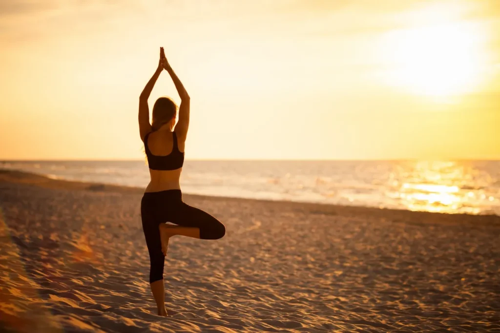 A woman is practicing yoga on the beach at sunset.