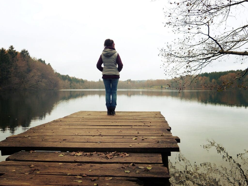 A woman experiencing menopause standing on a dock near a lake.