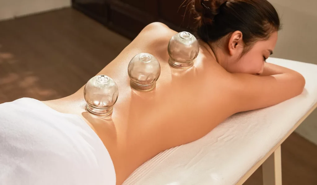 A woman is getting a massage with several glass bottles on her back.