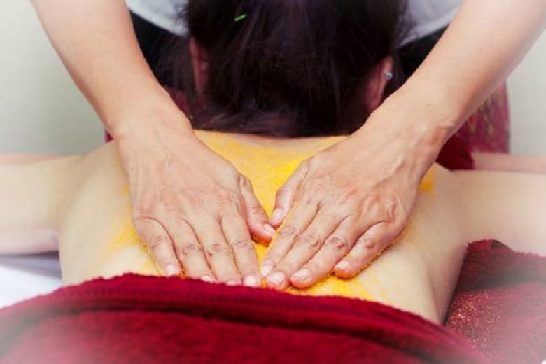 A woman getting a back pain massage with yellow powder.