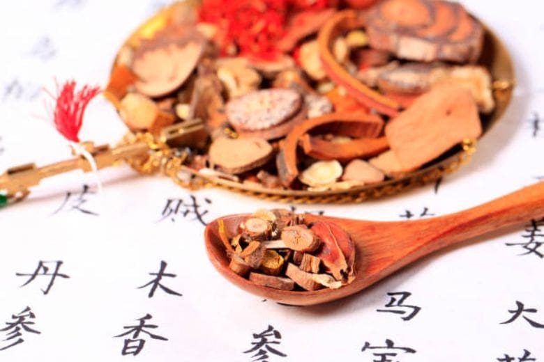 Traditional Chinese herbal medicine including licorice with a wooden spoon on paper with Chinese script.