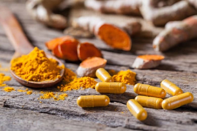 Tumeric capsules and tumeric powder for back pain on a wooden table.