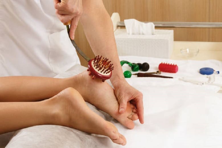 A person receiving a reflexology foot massage with various massage tools in the background.