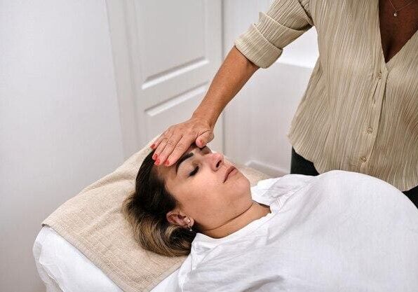 A woman lying down receiving a forehead massage from another woman in a serene, clinical setting.