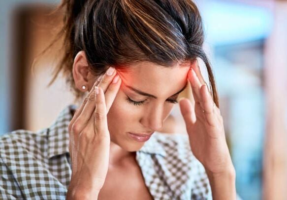 A woman is holding her head with her hands, possibly seeking relief from headaches or migraines.