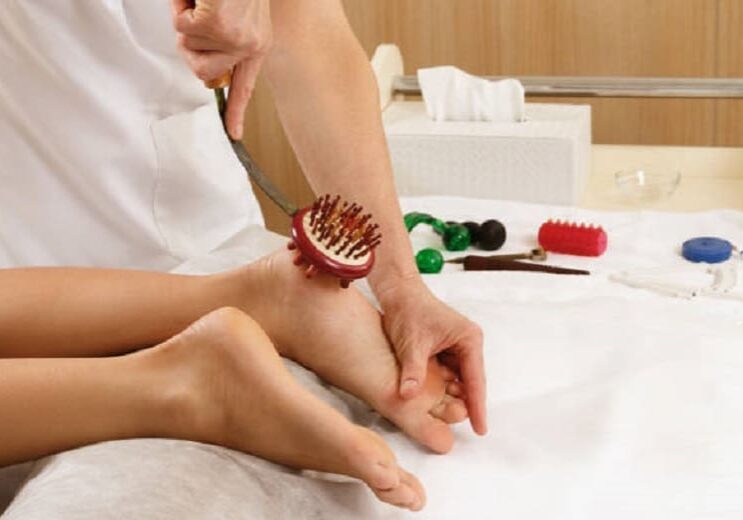 A person receiving a reflexology foot massage with various massage tools in the background.