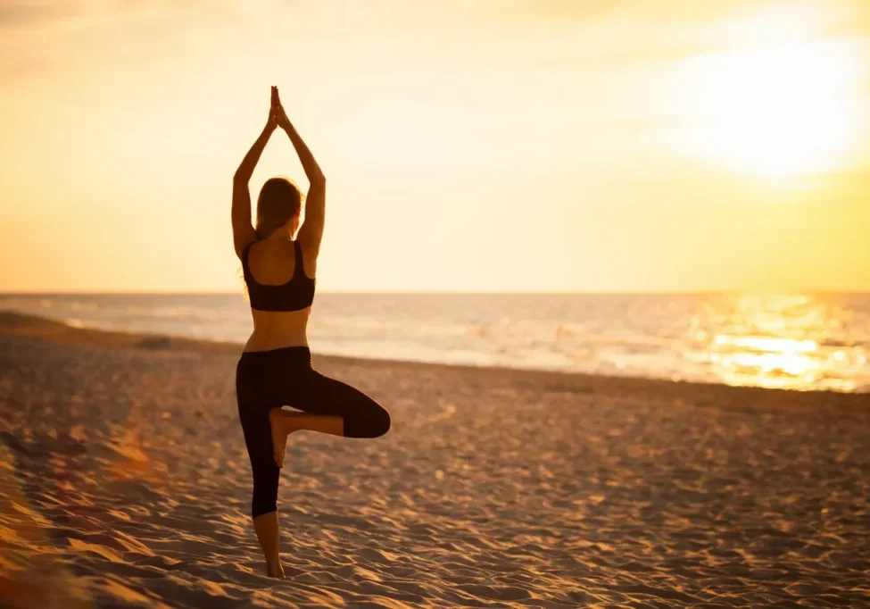 A woman is practicing yoga on the beach at sunset.